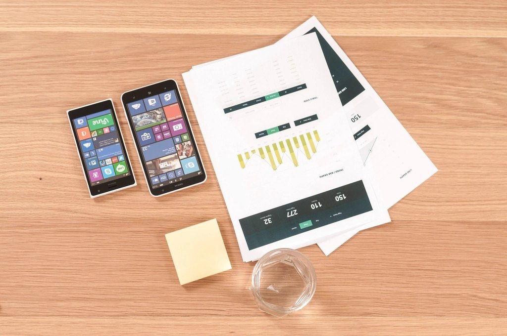 Two smartphones and printed interface designs on a wooden table